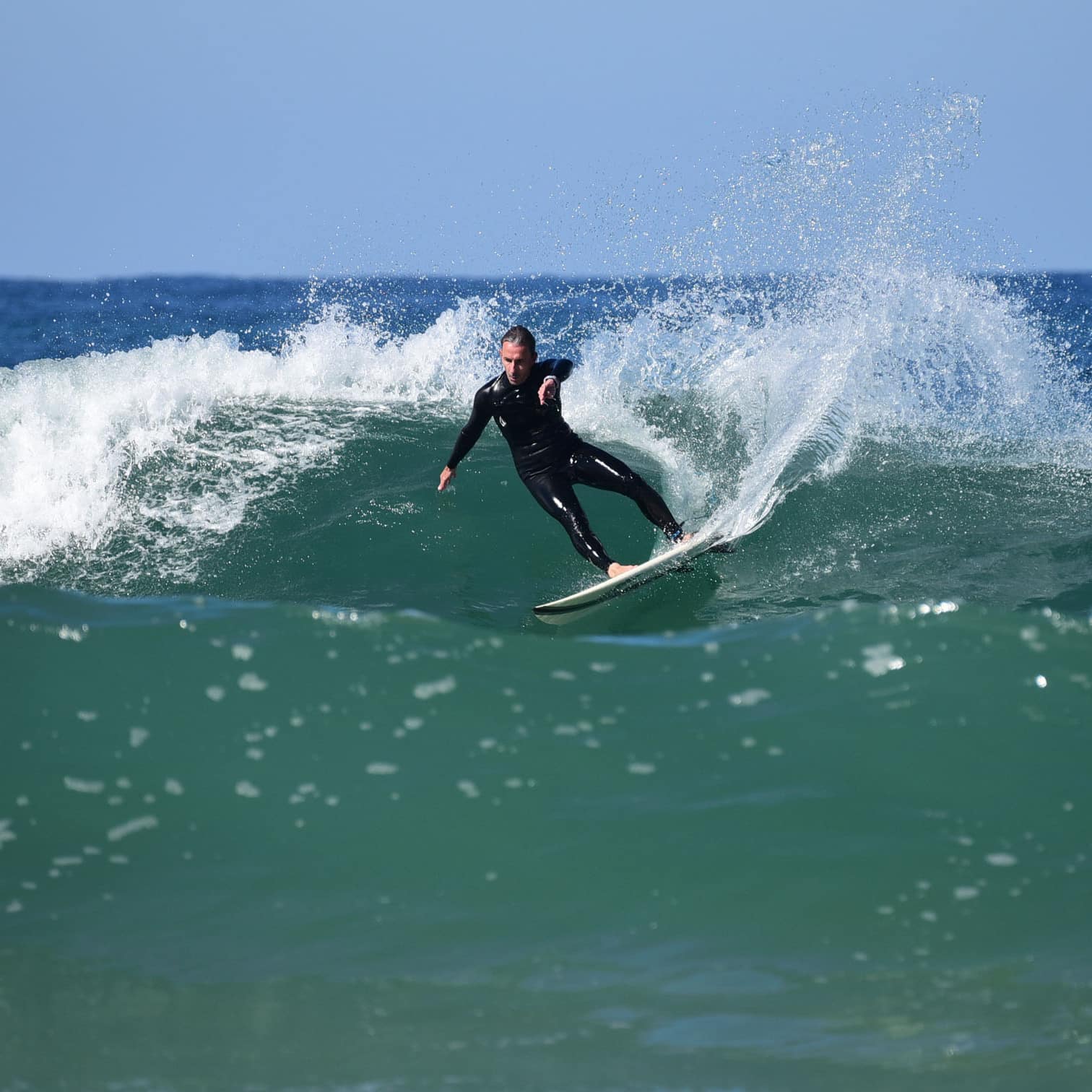 Surfeur concentré en combinaison noire réalisant un puissant virage, créant une gerbe d'eau sur une vague océanique.